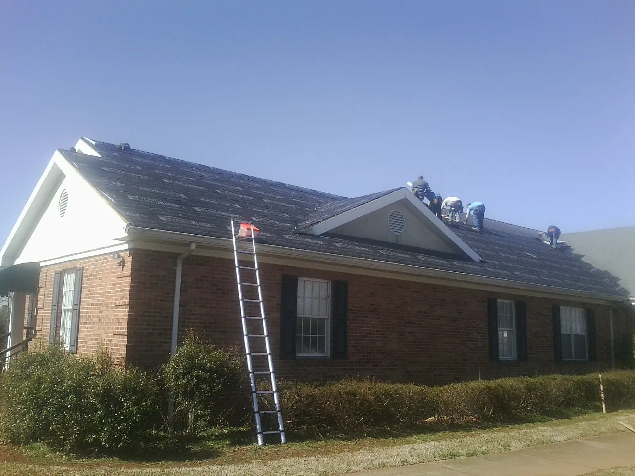Crew tearing shingles off a brick ranch roof with a ladder set — Metal Roof Repair work by our crew in Wilkesville