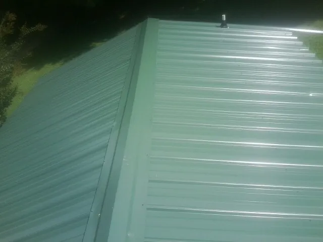New green metal panels meeting at the ridge of a roof — Flat Roof Repair work by our crew in Wilkesville
