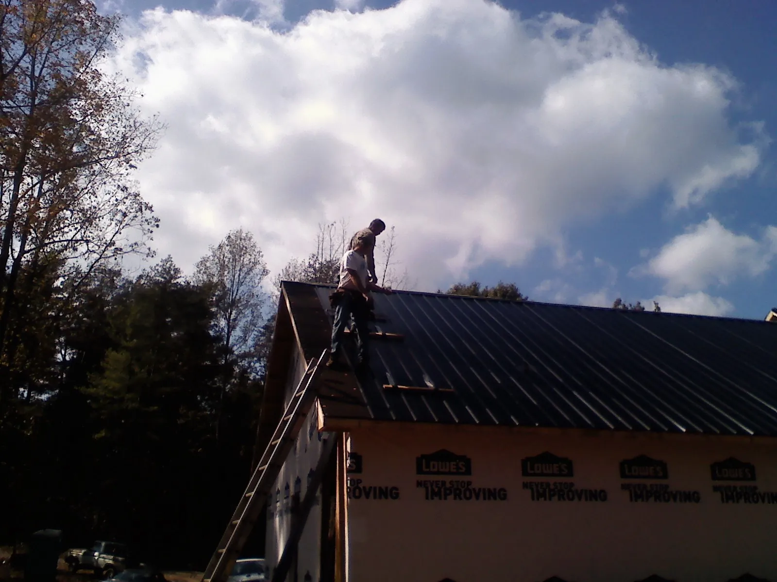 Roofer fastening dark metal panels high against a cloudy sky, from a Roof Inspection job in Wilkesville