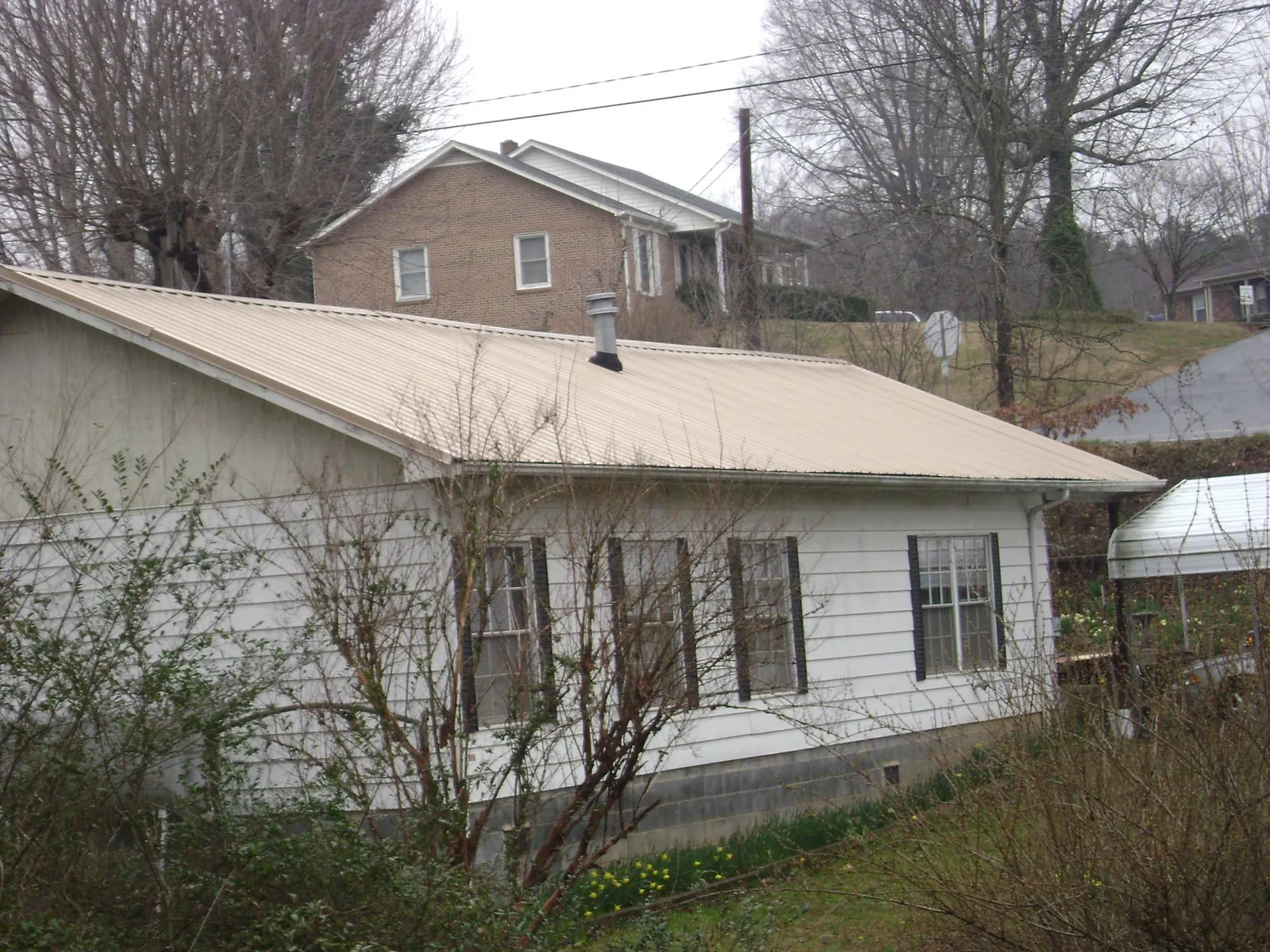Tan metal roof on a white sided house set into a hillside — Commercial Roofing by Roofing Brothers in Wilkesville